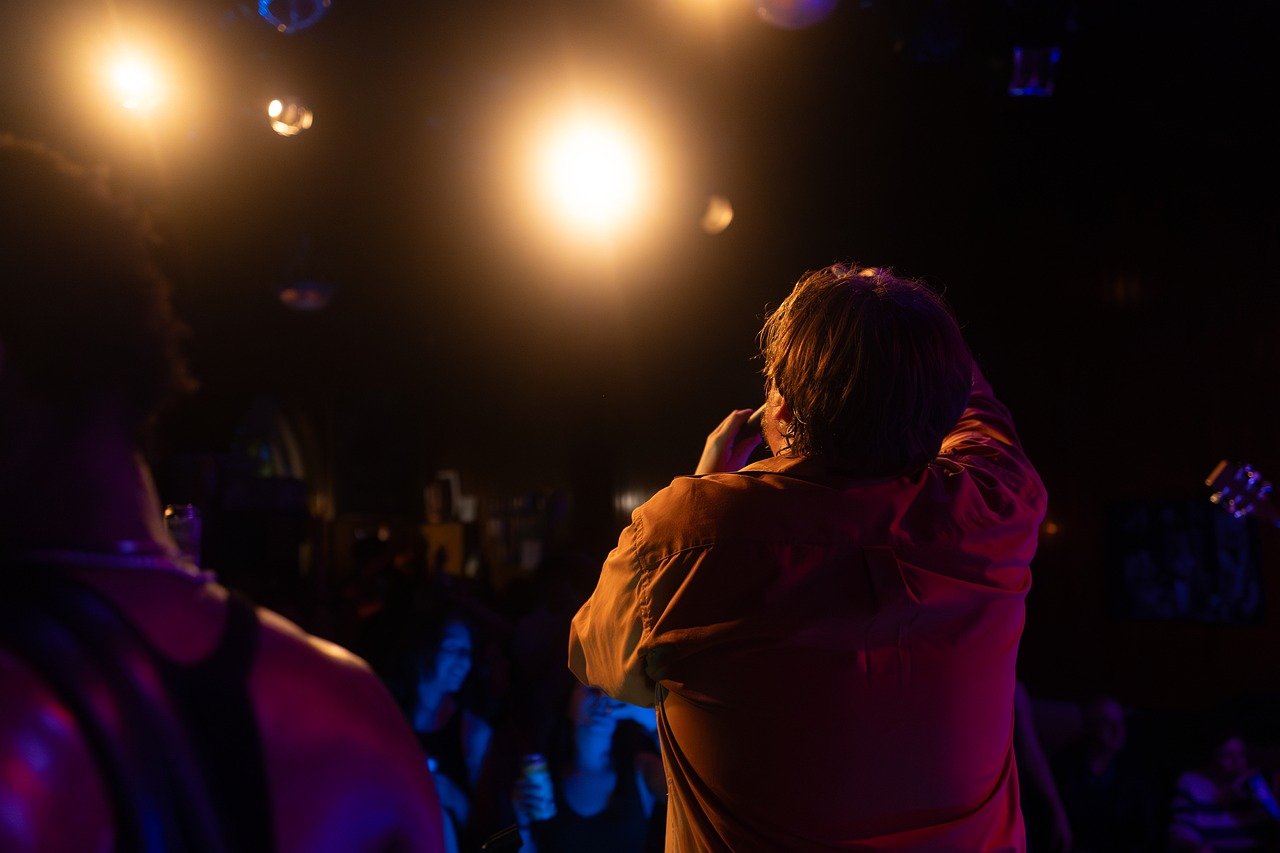 concert, singer, audience, stage, spotlight, orange, show, room, live music, entertainment, fans, atmosphere, music, microphone, energy, evening, podium, artist, performance, party, club